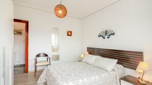 A bedroom with a bed, bedside tables, a chair, a hanging light fixture, and a wall decoration.