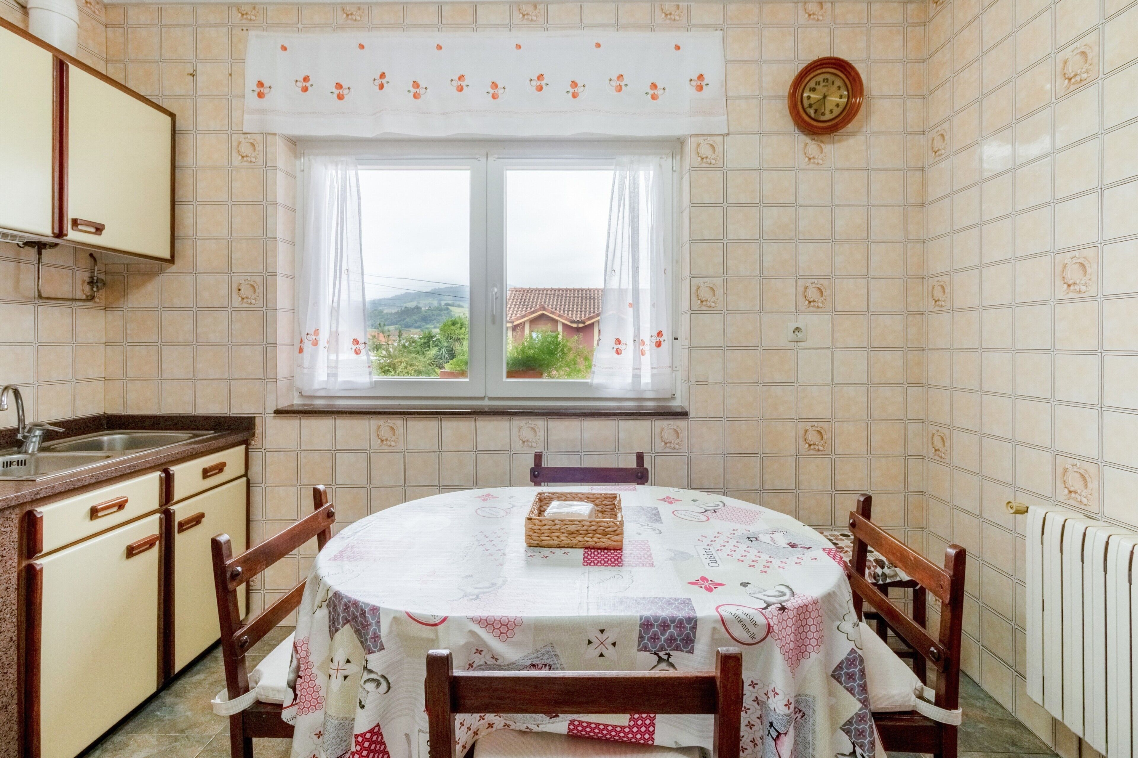 A kitchen with a round table, chairs, a window, and a clock on the wall.