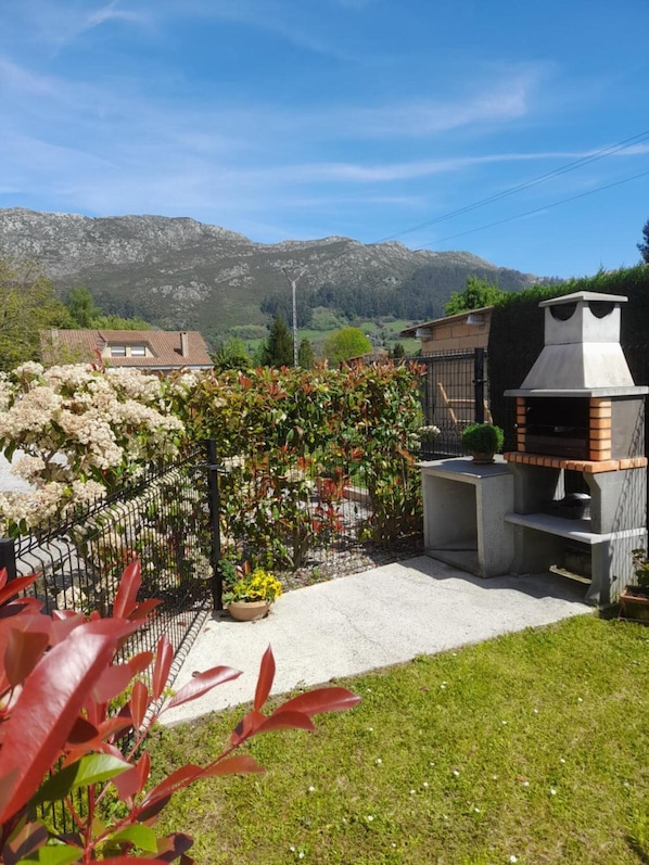A backyard with a barbecue grill, a fenced garden, and a mountain backdrop.