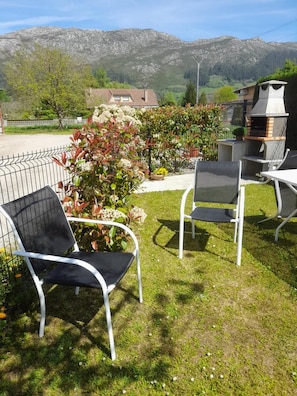 Eine Terrasse mit Gartenmöbeln, einem Grill und einem Garten mit Blumen und Sträuchern.