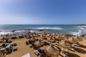 Een strand met ligbedden en rieten parasols.