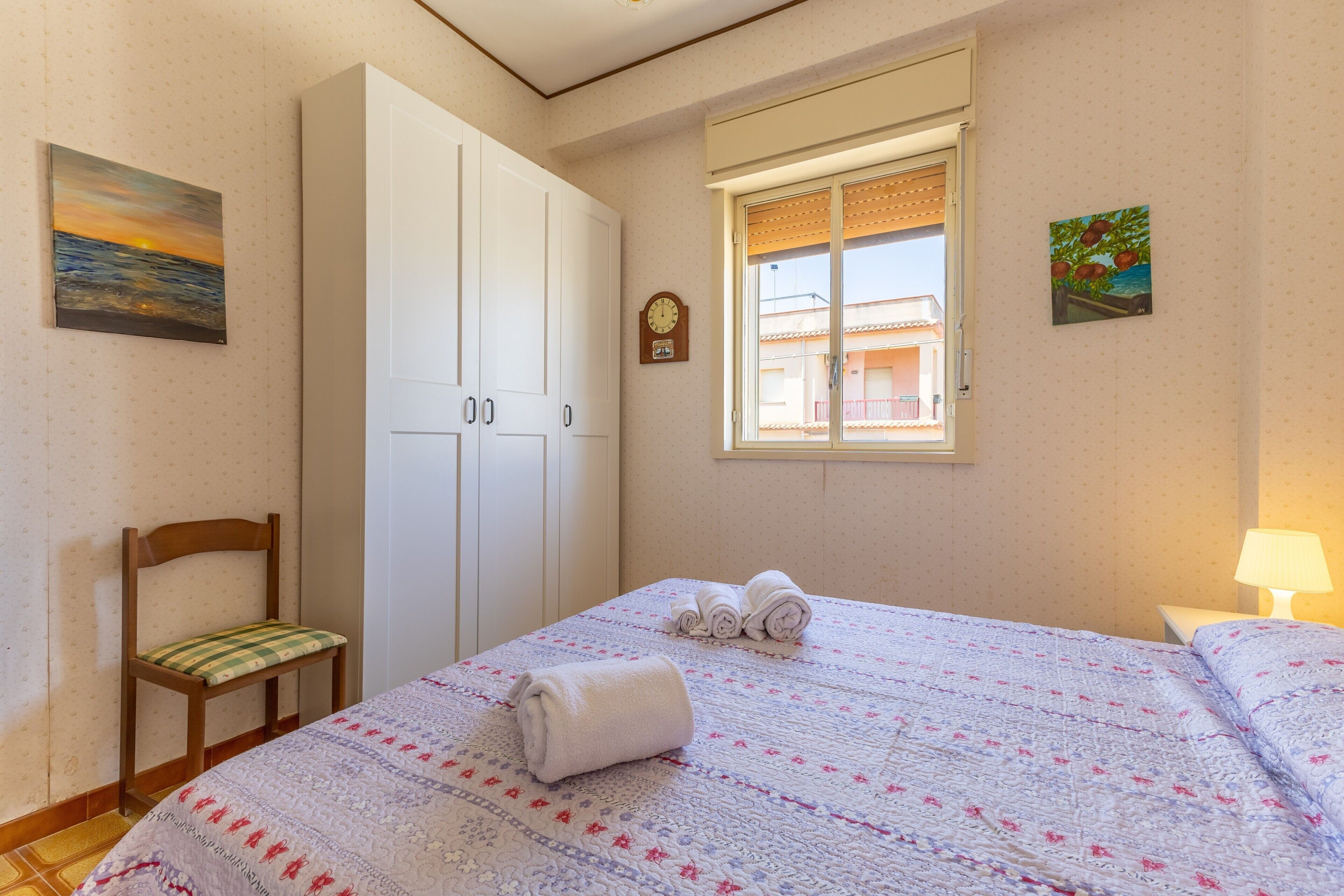 Quarto com cama, cadeira, guarda-roupa, janela e relógio de parede.