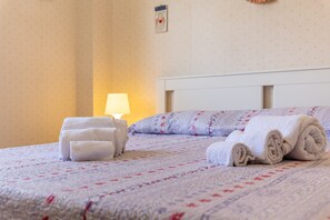 A neatly made bed with rolled towels, a bedside lamp, and a patterned wall.
