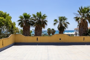 Eine Dachterrasse mit gelber Wand, Palmen und Blick auf das Meer.