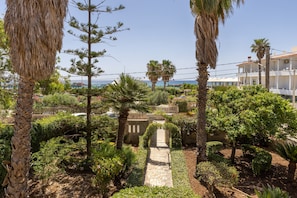Ein Garten mit Palmen, einem Kiesweg und Blick auf das Meer.