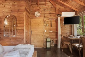 A wooden cabin interior with a bed, a desk, a television, and a shower area.