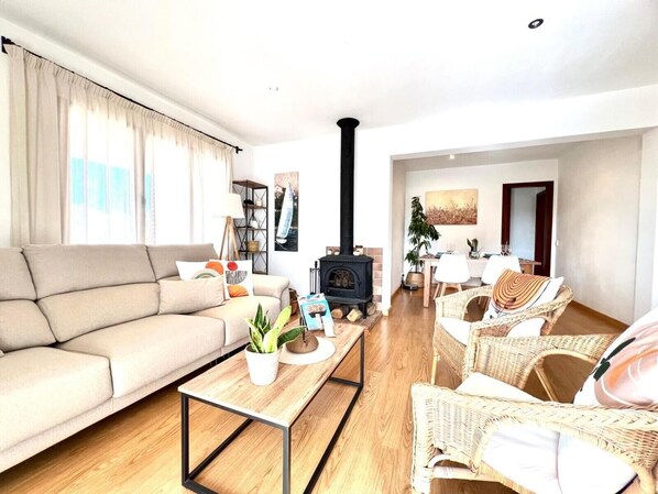 Una sala de estar con sofá, mesa de centro, sillas de mimbre, chimenea y comedor.