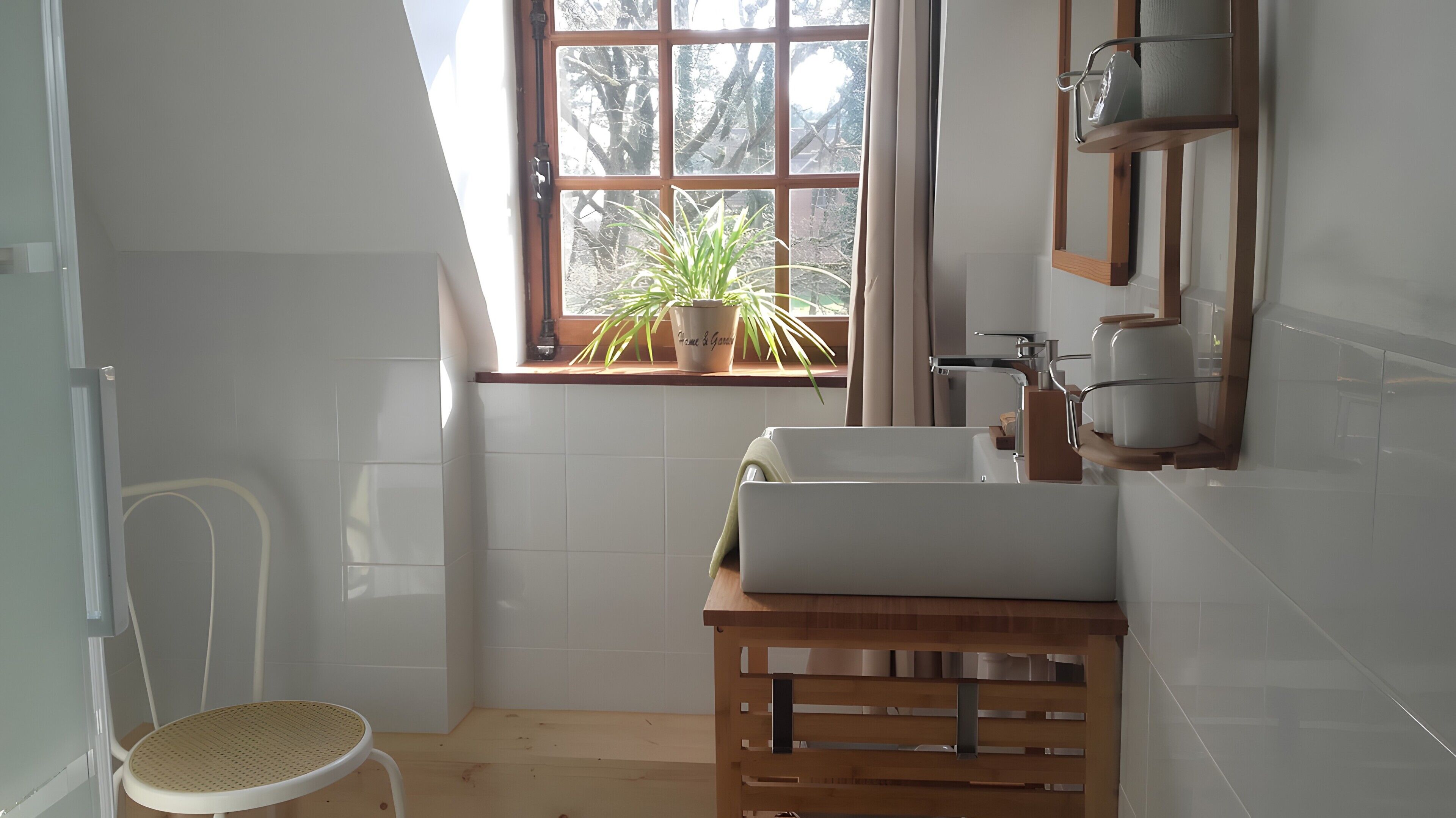Un baño con ventana, una planta en maceta, un lavamanos y una silla.