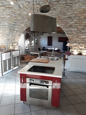 A kitchen with a built-in oven, a hanging light fixture, and a stone wall.