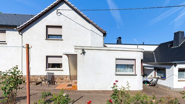 A two-story house with a sloped roof, a small attached garage, and a patio area with a table and chairs.