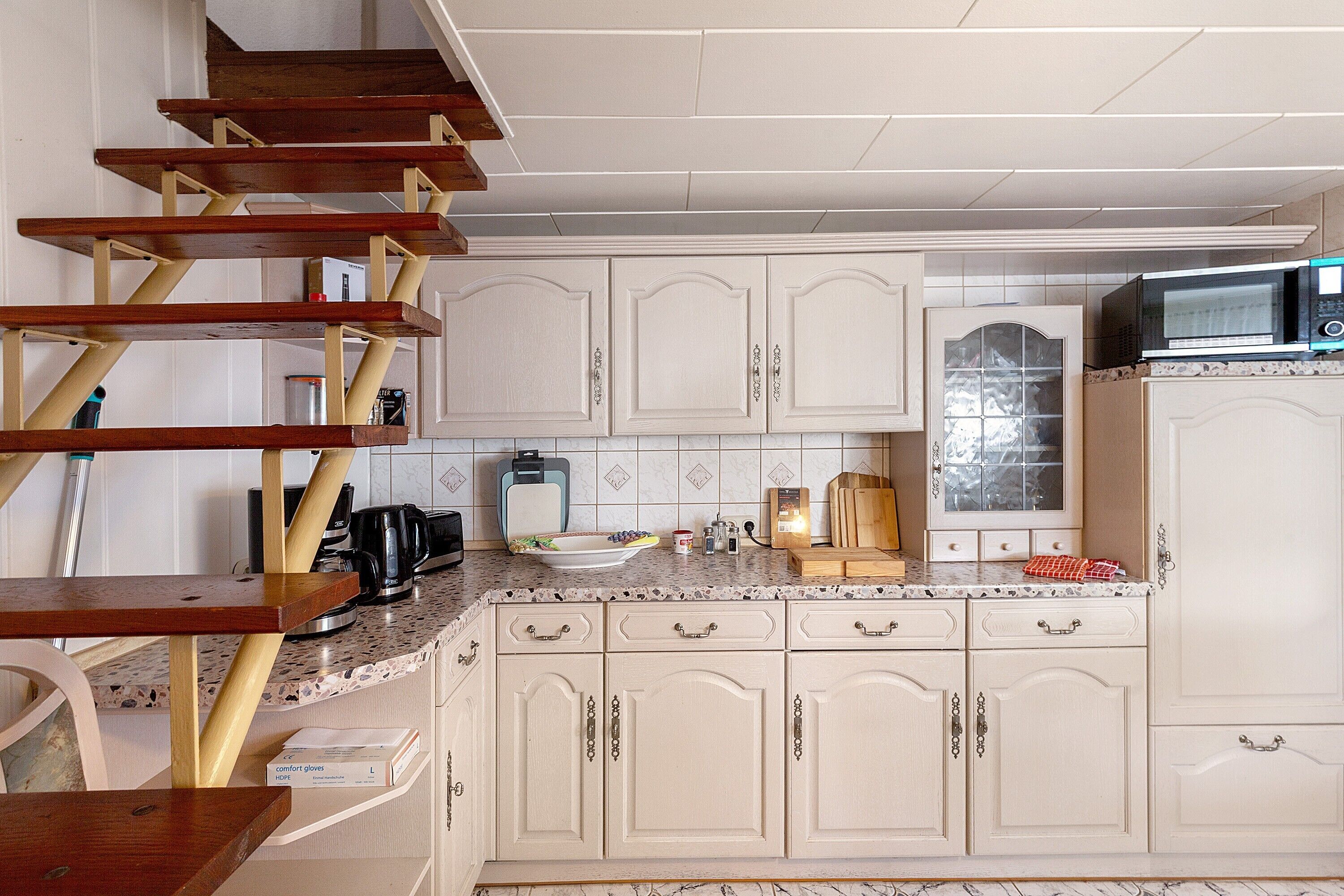 Una cocina con armarios blancos, microondas, cafetera y una escalera de madera.