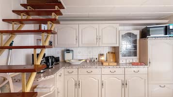 Una cocina con armarios blancos, microondas, cafetera y una escalera de madera.