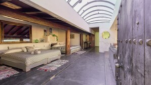 Un dormitorio con tragaluz, una cama grande, una puerta de madera y una mesita pequeña.