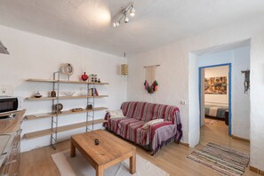 Sala de estar com sofá, mesa de madeira, estantes e área de cozinha com micro-ondas.