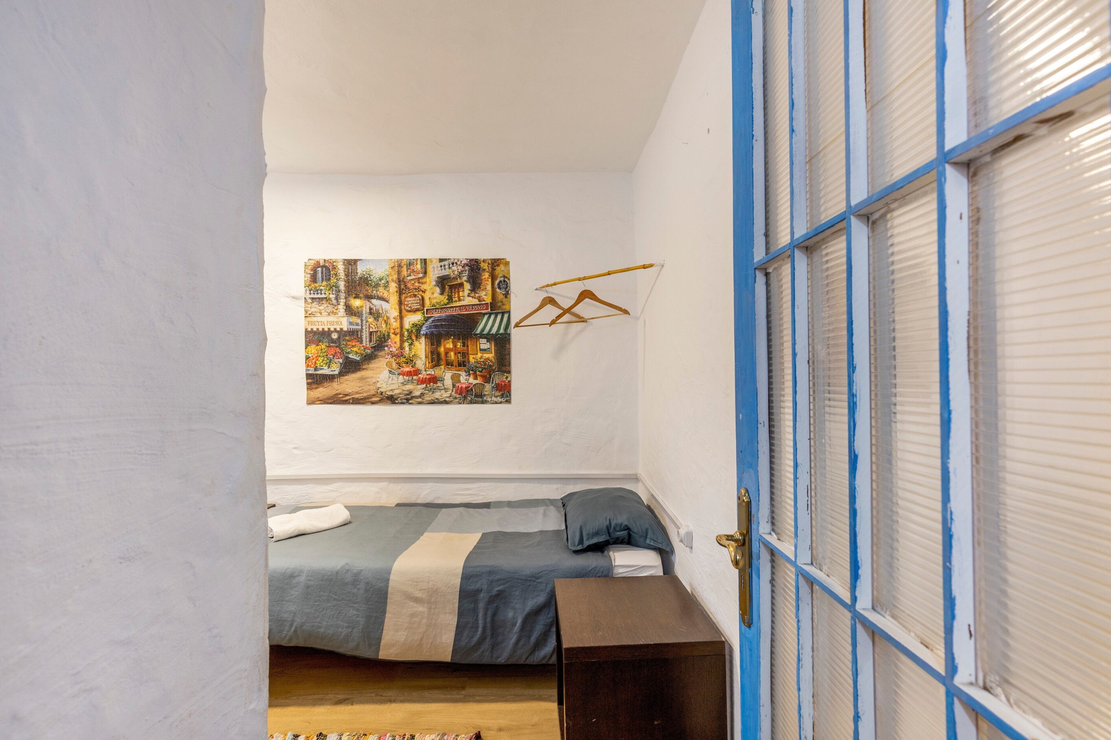 Ein Schlafzimmer mit einem Bett, einem Gemälde, einer hölzernen Bank und einer Tür mit blauer Umrandung.