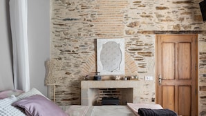 Een slaapkamer met een stenen muur, een houten deur, een open haard en een bed met kussens.