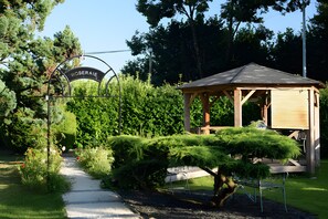 A garden with a wooden gazebo, a pathway, and a sign that reads 'ROSERAIE'.