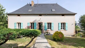 Een huis met twee verdiepingen, met een grindpad dat naar de ingang leidt, omringd door groen.