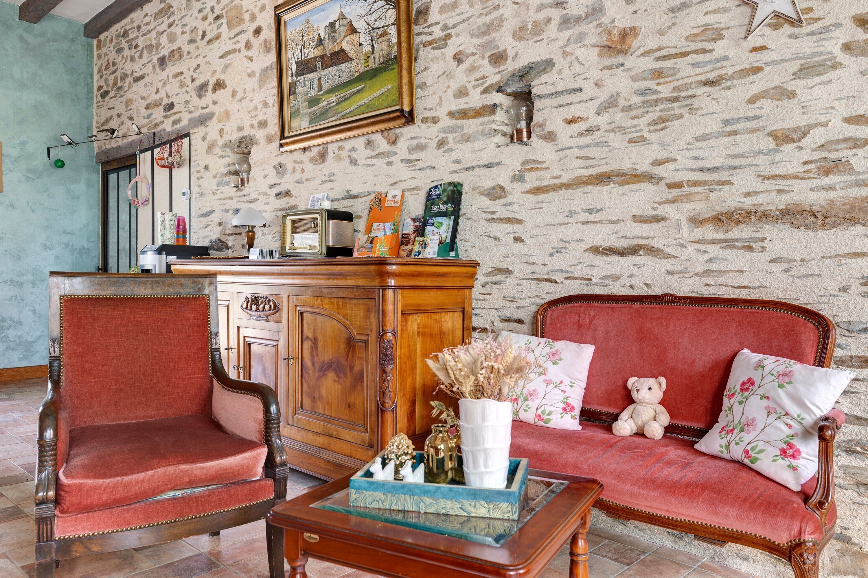 A room with a stone wall, a wooden cabinet, a red sofa, a wooden chair, and a small table with a vase and decorative items.