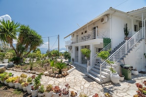 A white building with a balcony, a staircase, and a garden with various plants. - Room 'Ground Floor' with Sea View, Shared Pool and Wi-Fi (Nikiana)