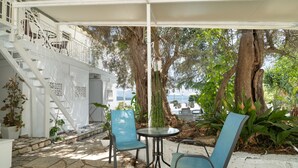 Un espace extérieur abrité, doté d’un sol en pierre, de deux chaises bleues, d’une petite table et d’un escalier menant à un niveau supérieur.