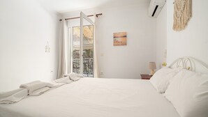 Une chambre avec un lit, une fenêtre, un climatiseur fixé au mur, une décoration murale en macramé et une petite table avec une lampe.
