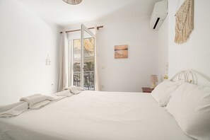 A bedroom with a bed, a window, a wall-mounted air conditioner, a macrame wall hanging, and a small table with a lamp. - Room '1st Floor' with Sea View, Shared Pool and Wi-Fi (Nikiana)