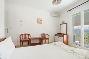 A bedroom with a bed, two wooden chairs, a small desk, a mirror, and a window with a view. - Room '1st Floor' with Sea View, Shared Pool and Wi-Fi (Nikiana)