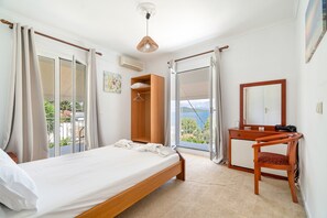 A bedroom with a bed, a wooden desk, a chair, a wardrobe, and a large window with a view. - Room '1st Floor' with Sea View, Shared Pool and Wi-Fi (Nikiana)
