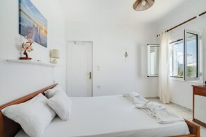 Ein Schlafzimmer mit einem Bett, einer Tür, einem Fenster mit Vorhängen, einer Wandlampe und einem Bild.