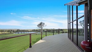 Una terraza de madera con vista a un campo cubierto de hierba y una masa de agua.