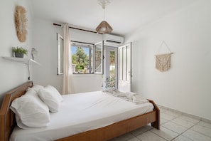 Ein Schlafzimmer mit einem hölzernen Bett, weißer Bettwäsche, einem Deckenventilator, einer Topfpflanze und einem Wandbehang aus Makramee.