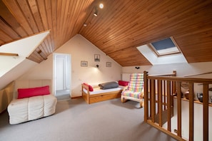 Ein Schlafzimmer im Loft-Stil mit geneigter Decke, einem Oberlicht, einem Bett, einem Sessel und einem Holgeländer.