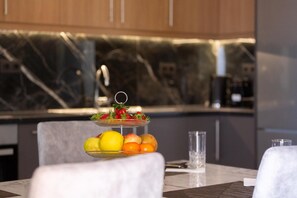 A three-tiered fruit stand with apples, oranges, and a bowl of strawberries on a marble countertop in a modern kitchen. - Marina A1 Apartment with Jacuzzi, Sea View, Wi-Fi and Air Conditioning (Kardamyli)