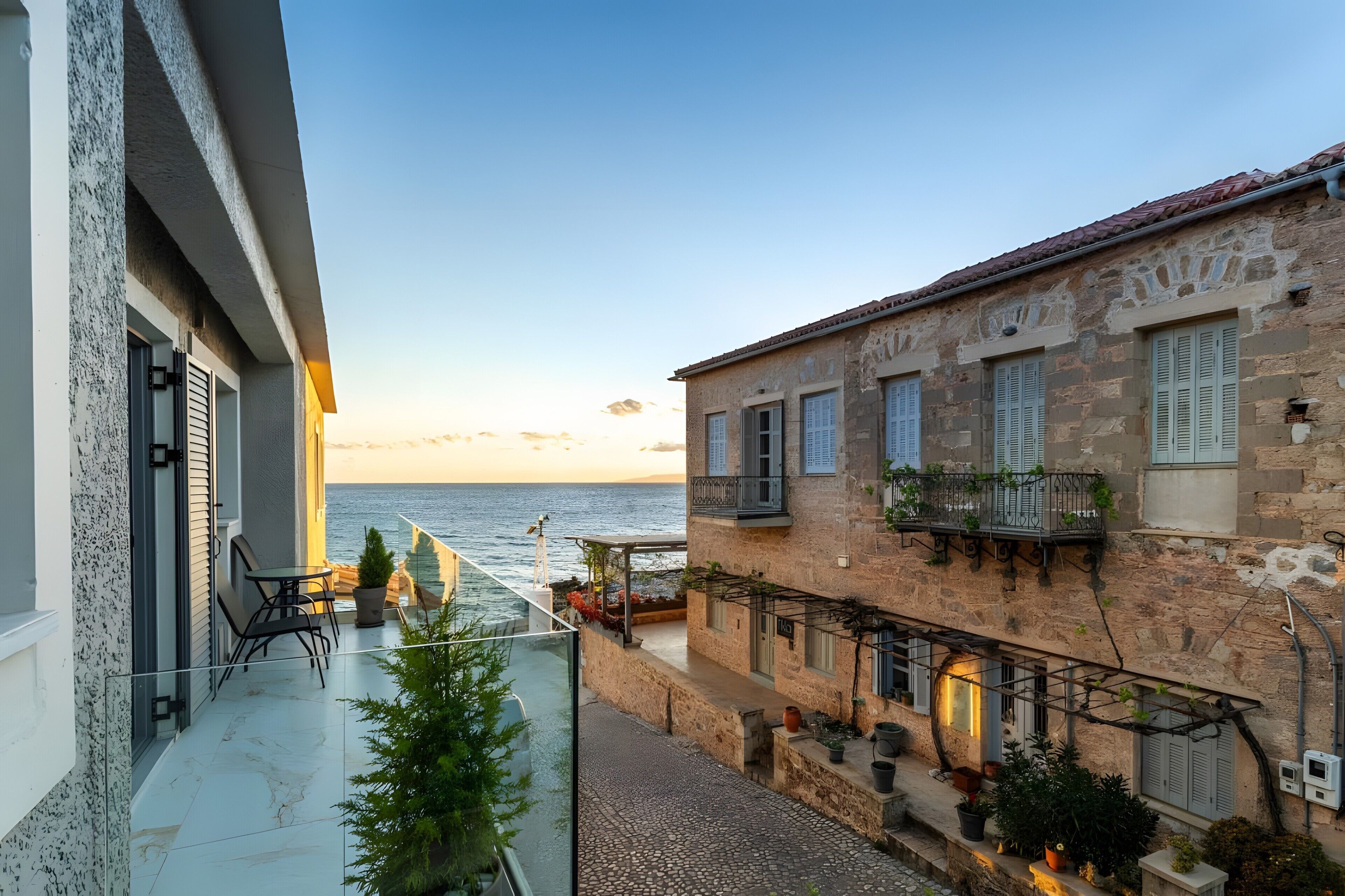 Ein Küstenhaus mit Balkon und Meerblick, Steinmauern und einer kleinen Außenbereich-Sitzgelegenheit.