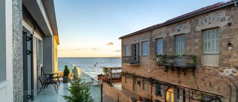 Ein Küstenhaus mit Balkon und Meerblick, Steinmauern und einer kleinen Außenbereich-Sitzgelegenheit.