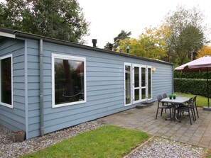 A small, single-story building with a patio area featuring a table and chairs, a covered outdoor seating area, and a small garden with a hedge. - Velthorst Sauna 4 (Brunssum)