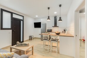 Eine kompakte Küche mit Kochinsel, Barhocker, einem kleinen Tisch und einem an der Wand montierten Fernseher.