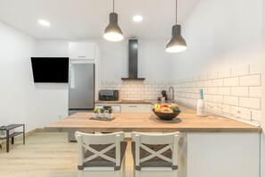 Eine moderne Küche mit einer Holztischinsel, zwei Pendelleuchten, einer eingebauten Mikrowelle und einem an der Wand montierten Fernseher.