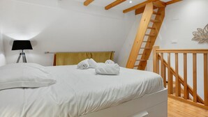 Et soveværelse med seng, lampe, en træstige og en dekorativt ophængt vægkunst.
