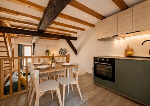 Una cocina moderna con vigas de madera, un comedor con sillas blancas y un horno empotrado.