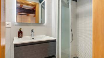 Une salle de bain avec un lavabo blanc, un miroir, un flacon de savon liquide et un espace douche.