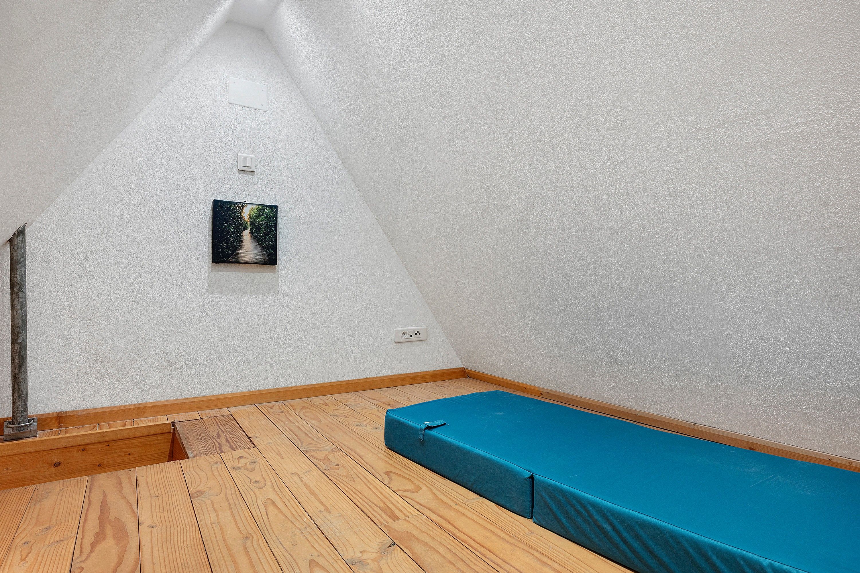 Une pièce étroite avec un plancher en bois, un banc bleu et un petit tableau encadré accroché au mur.