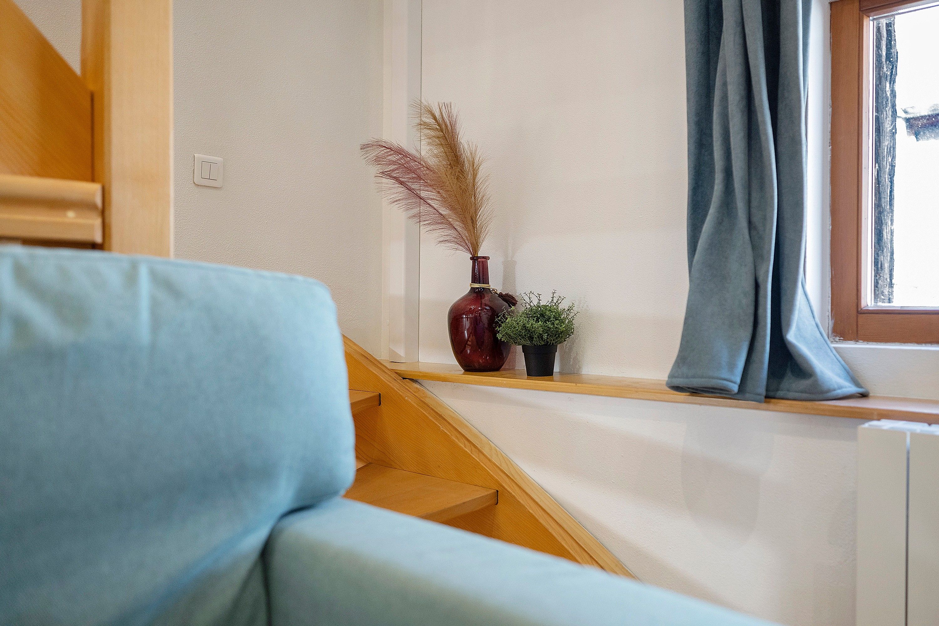 A staircase leading to a landing with a blue curtain, a wooden railing, and a small potted plant.