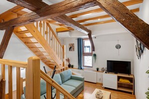 Un salón acogedor con una escalera de madera, un sofá, un televisor y una ventana con cortinas.