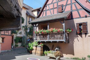 Una casa tradicional con entramado de madera y un balcón decorado con flores, una calle adoquinada y un barril rústico.