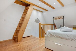 Un dormitorio con escalera de madera, cama con ropa blanca, radiador y ventilador de pared.