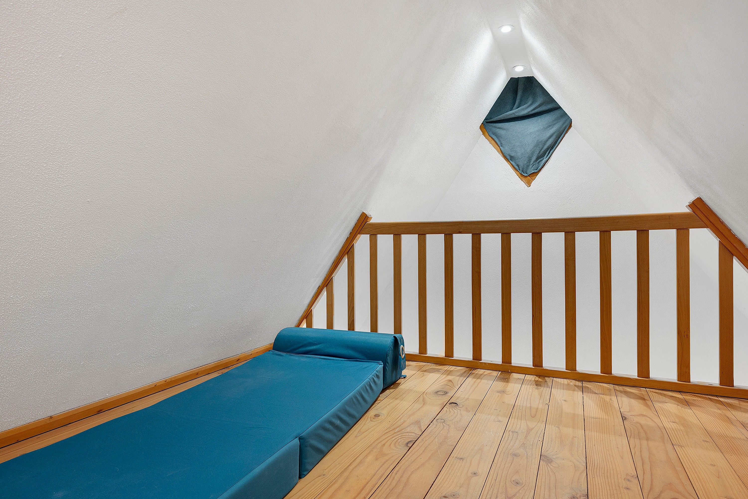 Een knus, klein kamertje met een houten vloer, een enkel bed met blauw beddengoed en een schuin dak met dakraam.