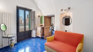 Een kamer met een blauwe betegelde vloer, een houten deur, een vintage dressoir, een rode bank en een spiegel aan de muur.