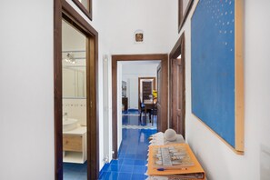 Un couloir avec un sol carrelé de carreaux bleus, un cadre de porte en bois, un tableau d’affichage et une table sur laquelle se trouvent des papiers et un ballon.